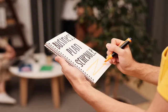 Close-up of a hand writing in a notebook with 'Business Plan Schedule' indoors. Subscription commerce planning: offer, margin and compliance